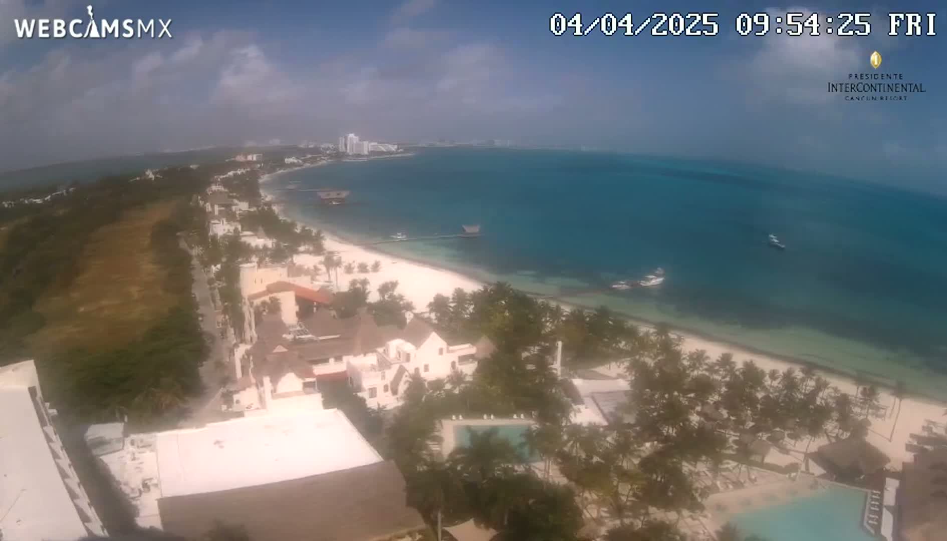 An aerial view shows a resort town on a tropical beach with clear skies and calm turquoise water.