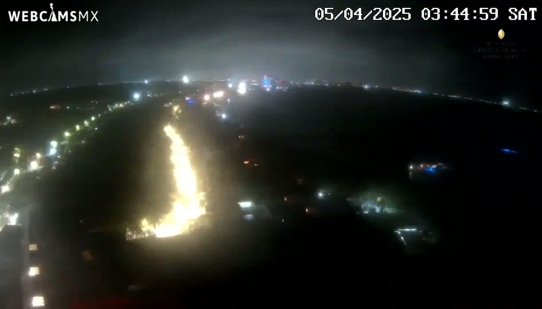 A nighttime aerial view shows a long, bright streak of light, possibly a fire or other intense illumination, extending through a dark landscape with scattered lights.