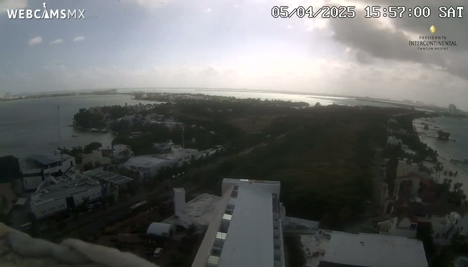 An elevated view shows a coastal area with buildings and vegetation under partly cloudy skies.