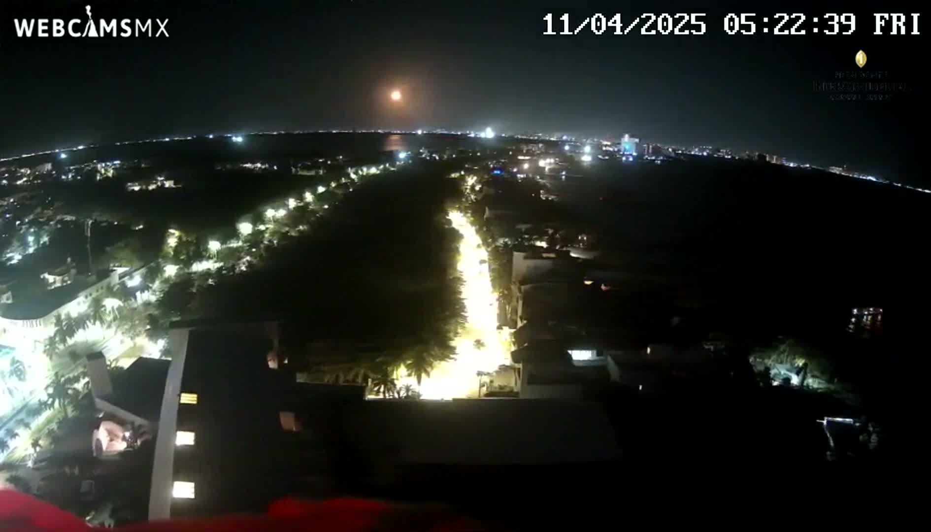 A nighttime aerial view of a city with a brightly lit street running through it, under a clear sky with a bright moon or planet visible.