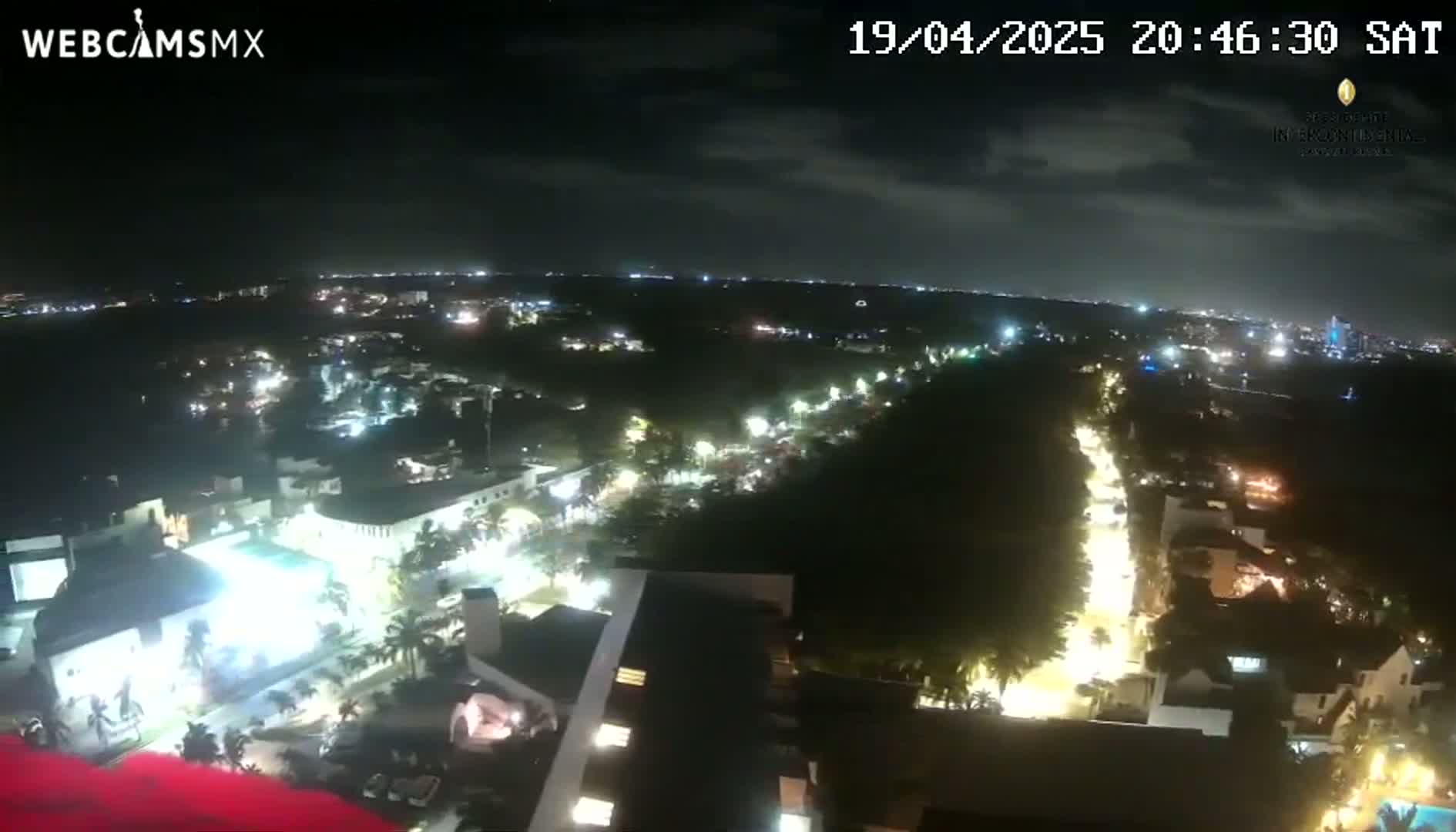 A nighttime aerial view of a city shows illuminated streets and buildings under a partly cloudy sky.