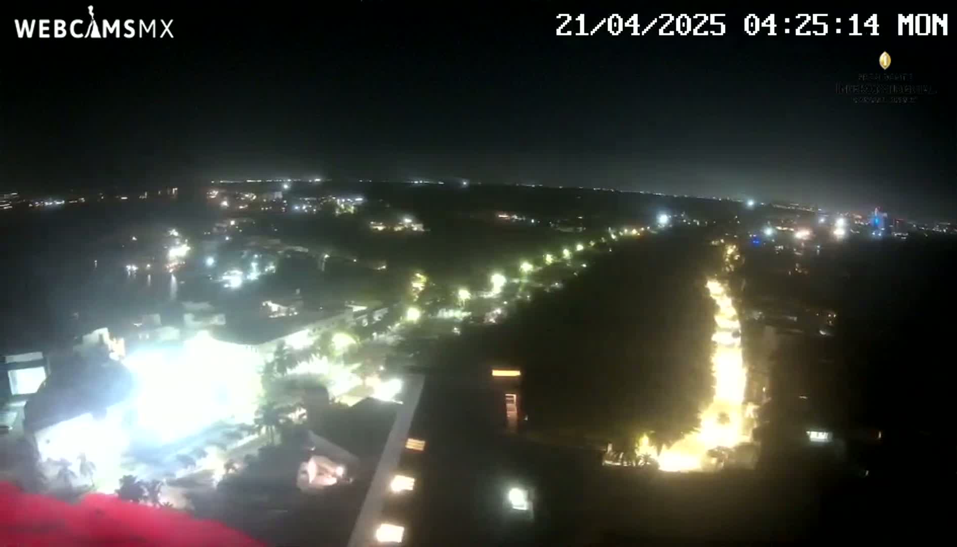 A nighttime aerial view shows a city illuminated with lights, featuring a long, brightly lit road cutting through a dark, tree-covered area.