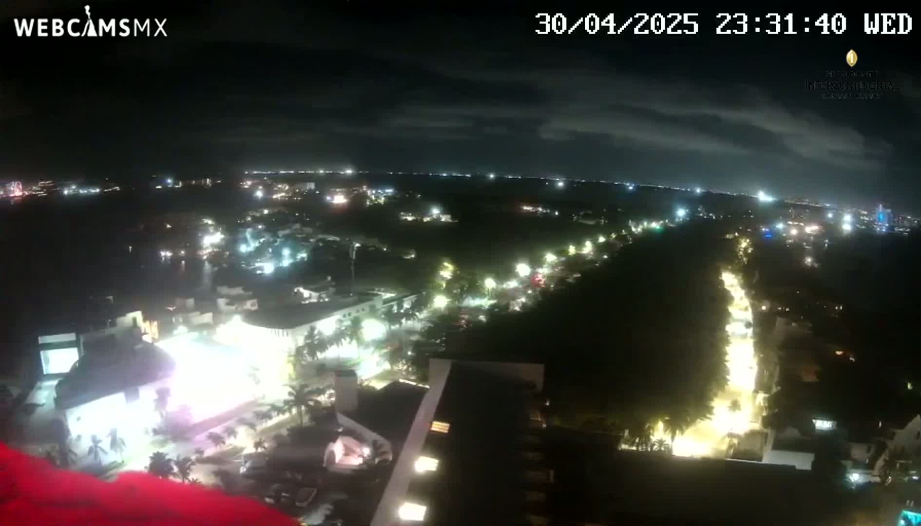 A nighttime aerial view of a city with brightly lit streets and buildings under a partly cloudy sky.