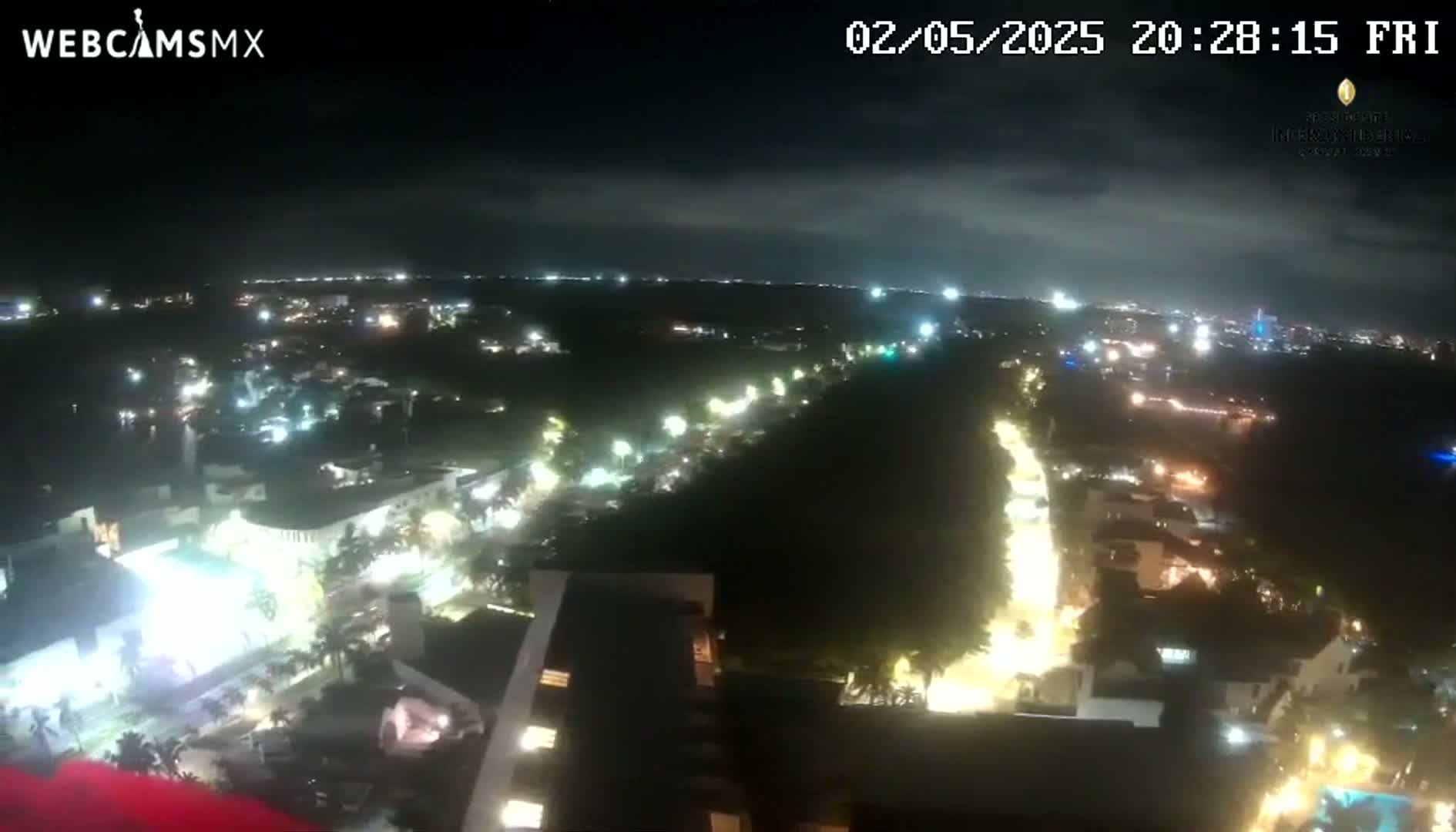 A nighttime aerial view shows a city with illuminated streets and buildings under a partly cloudy sky.
