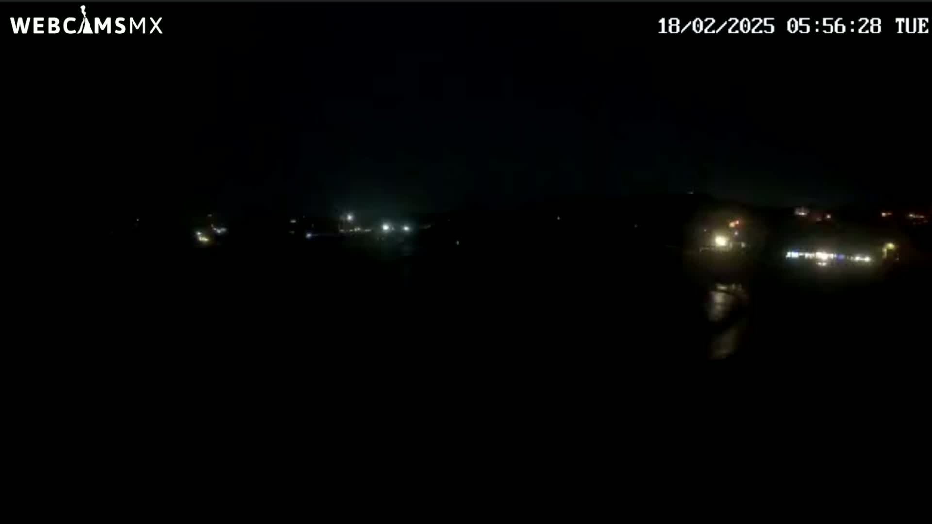 At night, faint lights from a distant town or buildings are visible across a dark landscape.
