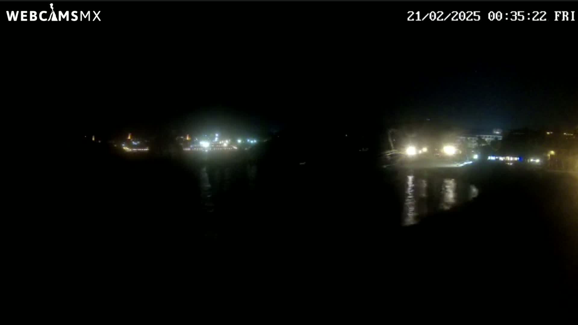 A nighttime, low-light view of a body of water with dimly lit buildings and vehicles visible in the distance.