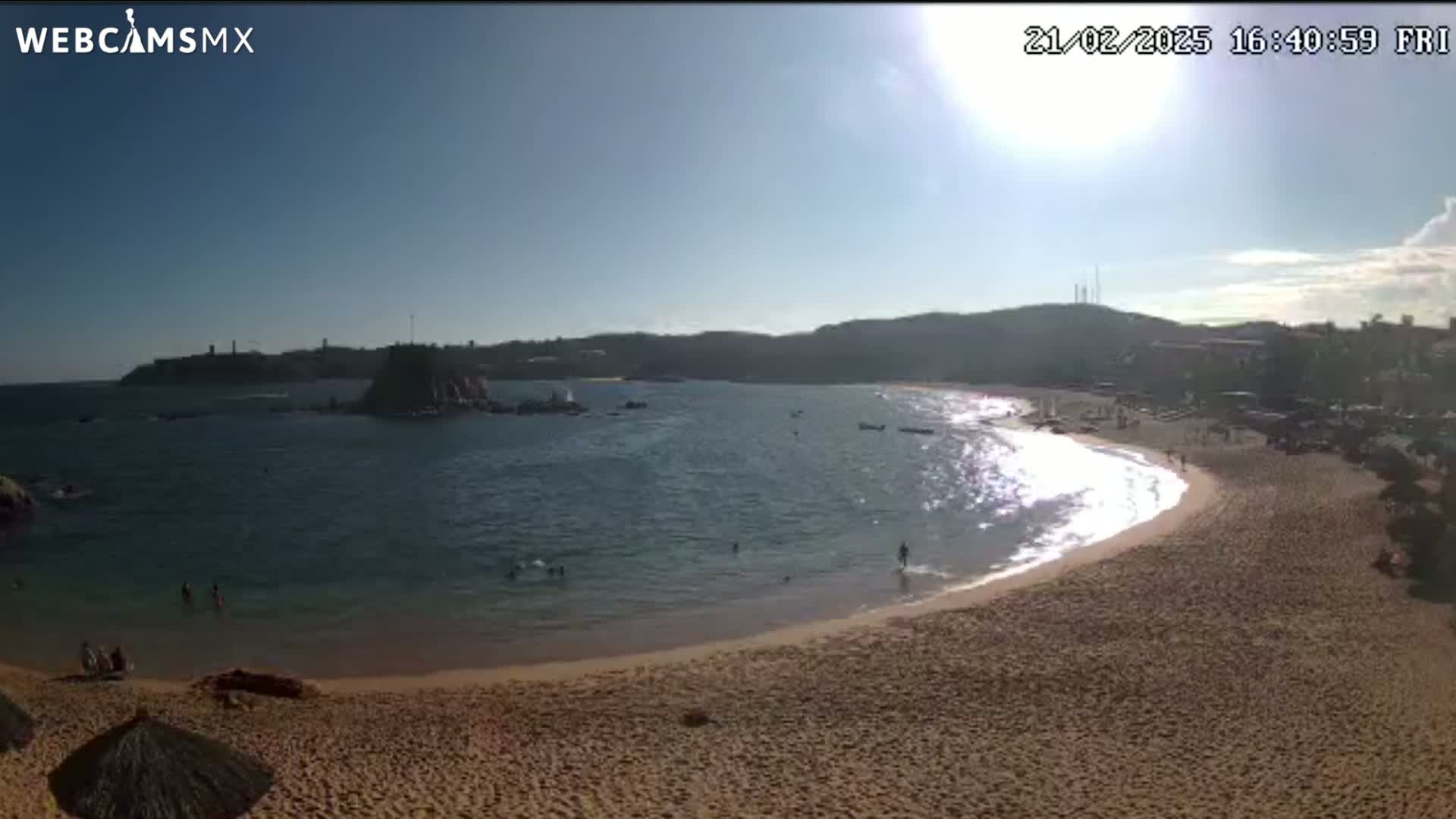 A sunny day at a secluded beach cove with calm water, a sandy shore, and a few people swimming and relaxing.