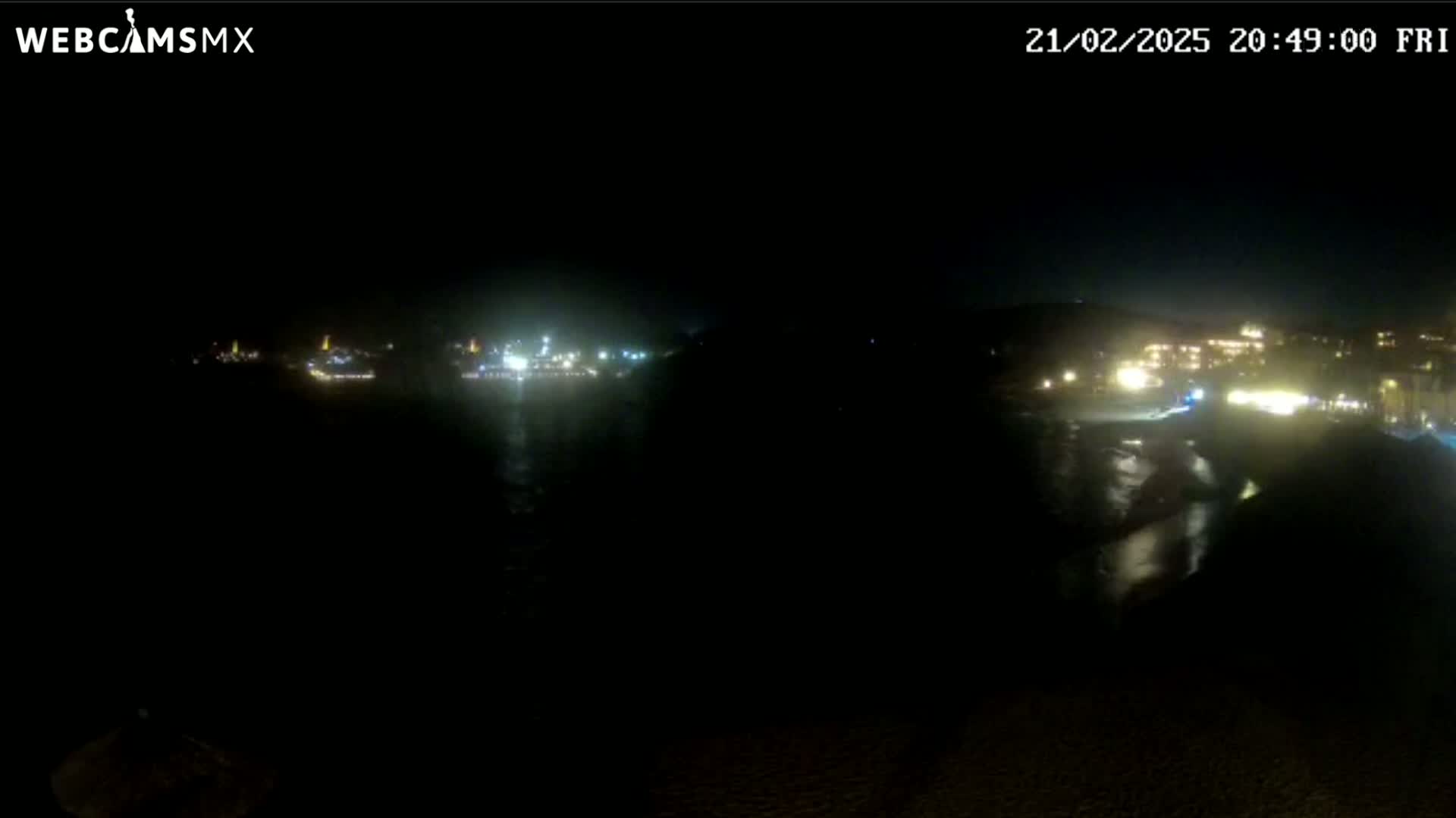 A nighttime view of a coastline with dimly lit buildings and a dark body of water.