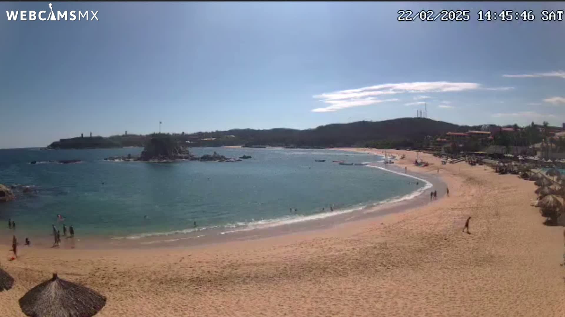 A sunny day at a secluded beach cove, with calm, clear water lapping a sandy shore where several people are swimming and relaxing.
