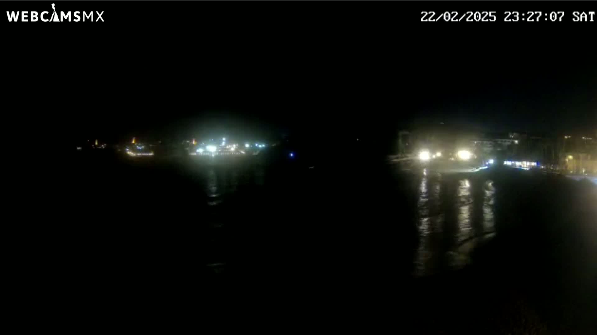 A nighttime view of a dark body of water with dimly lit buildings and lights reflecting on the water's surface.