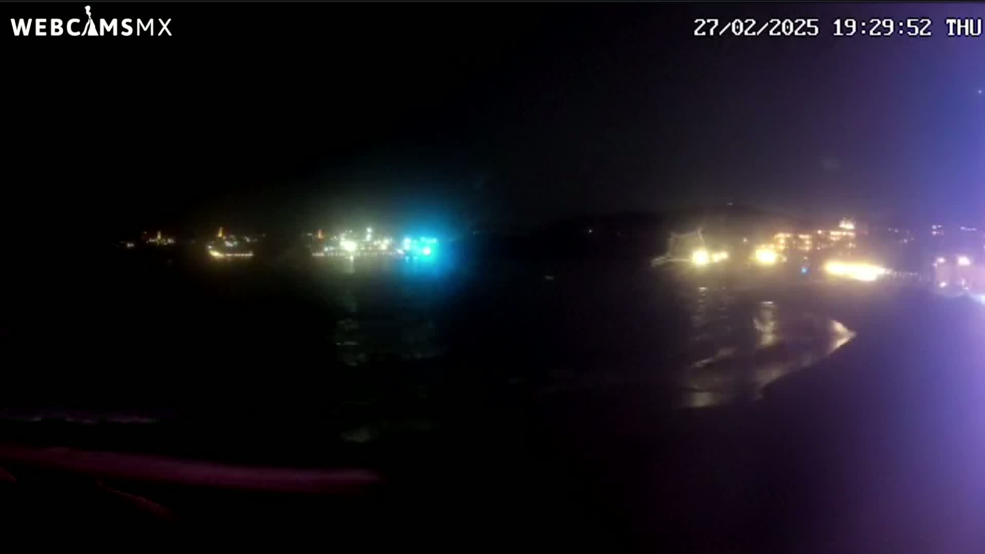A nighttime view of a dark body of water with illuminated areas on both shores.