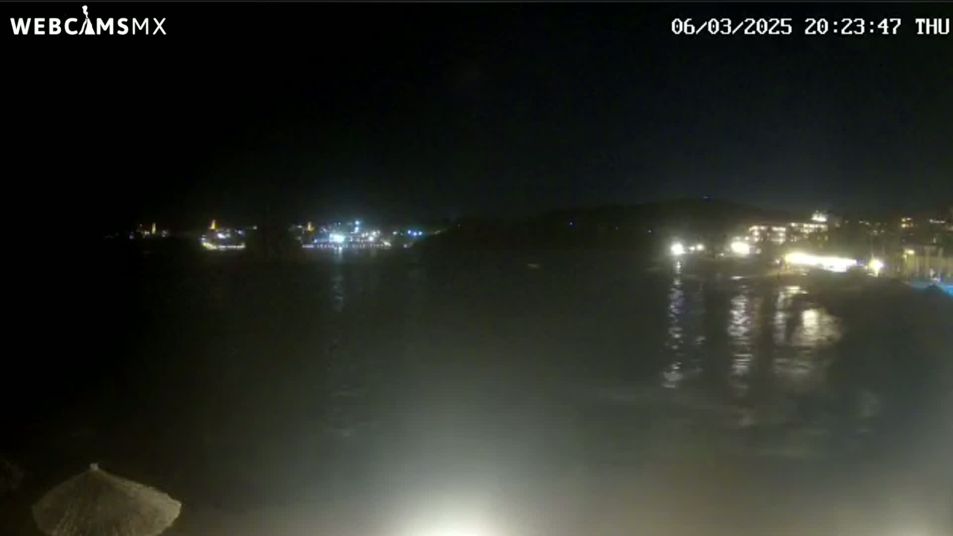 A nighttime view of a dark body of water reflecting the lights of buildings on the opposite shore under a clear, dark sky.