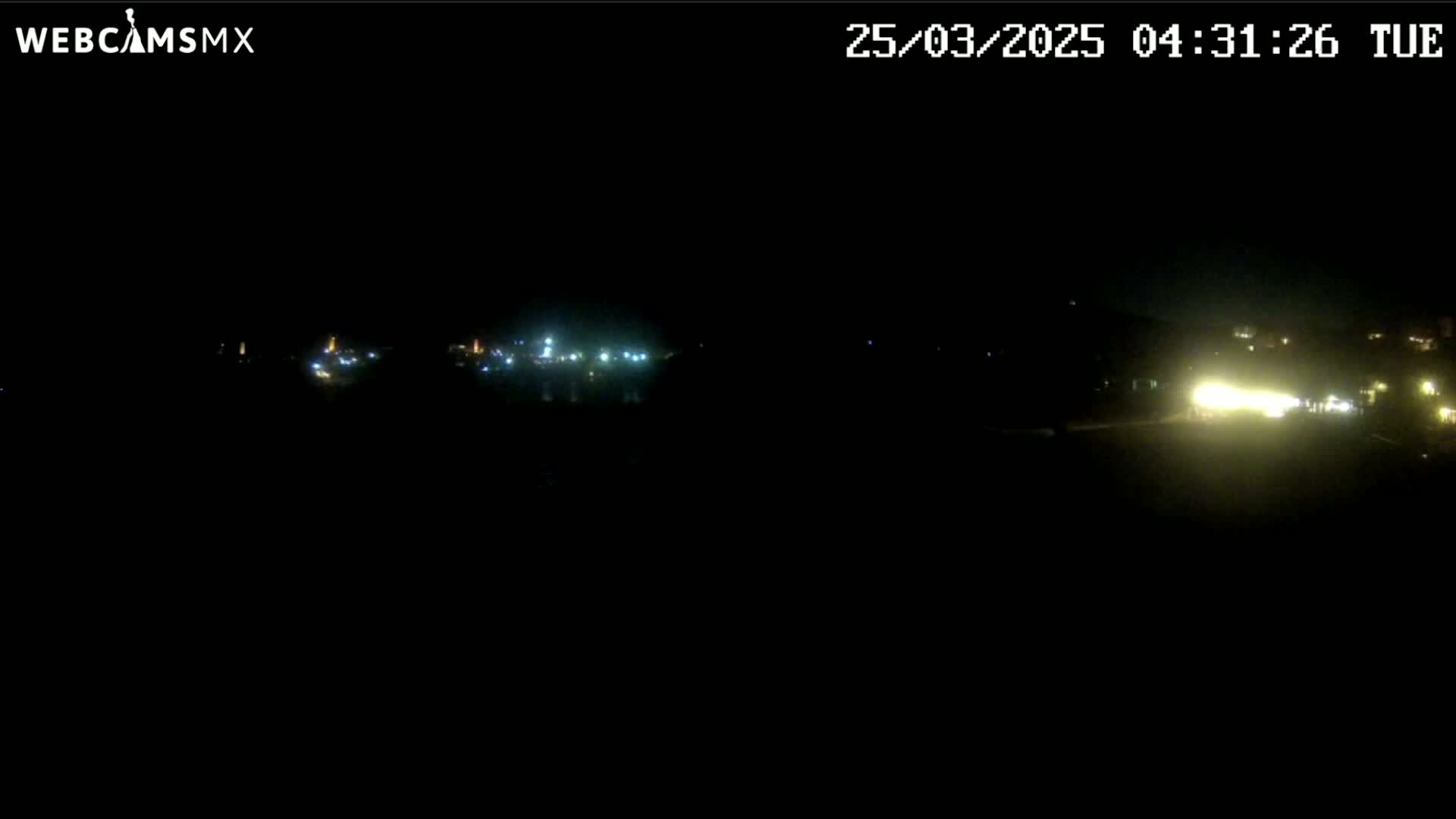 At night, faint lights from a distant town or city are visible against a dark, mostly obscured landscape.