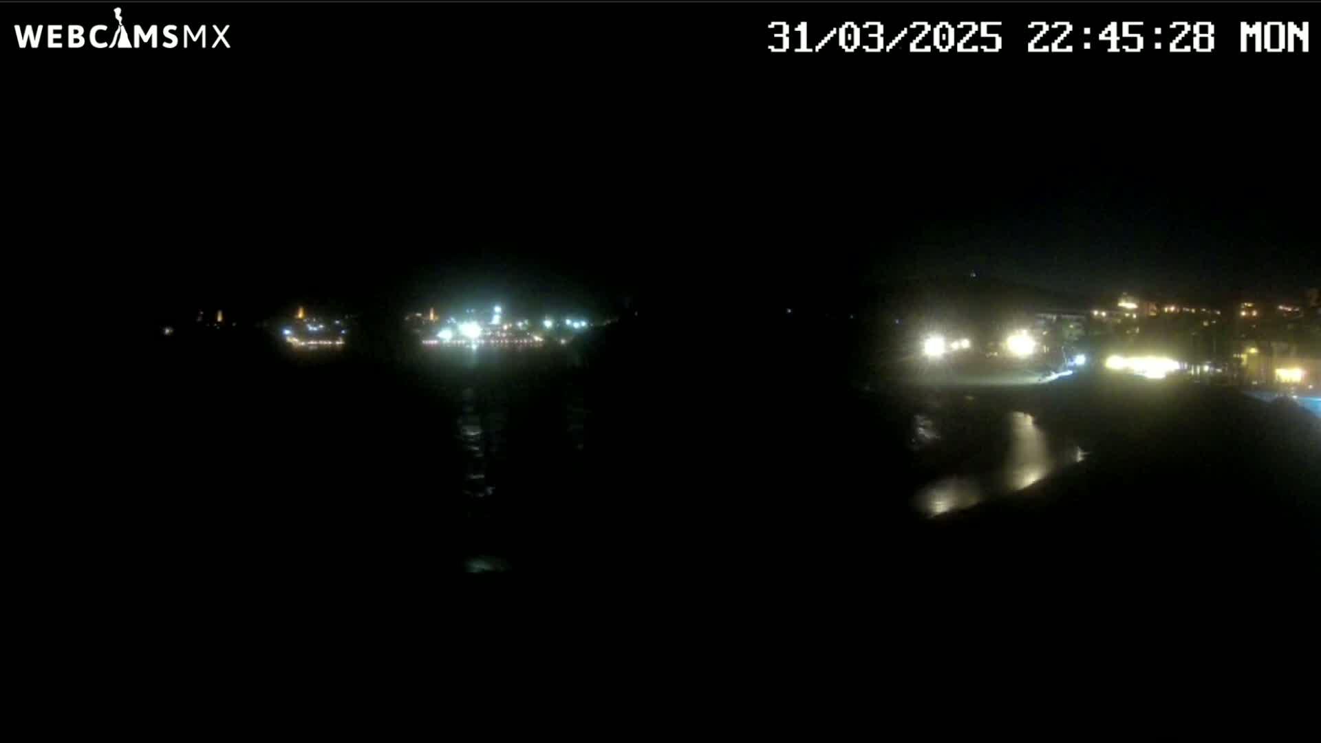 A nighttime long shot of a dark body of water reflecting the lights of a distant city.