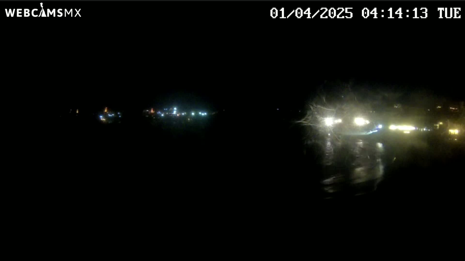A nighttime, blurry view of a roadway with several distant lights and some vehicle headlights visible in the foreground.