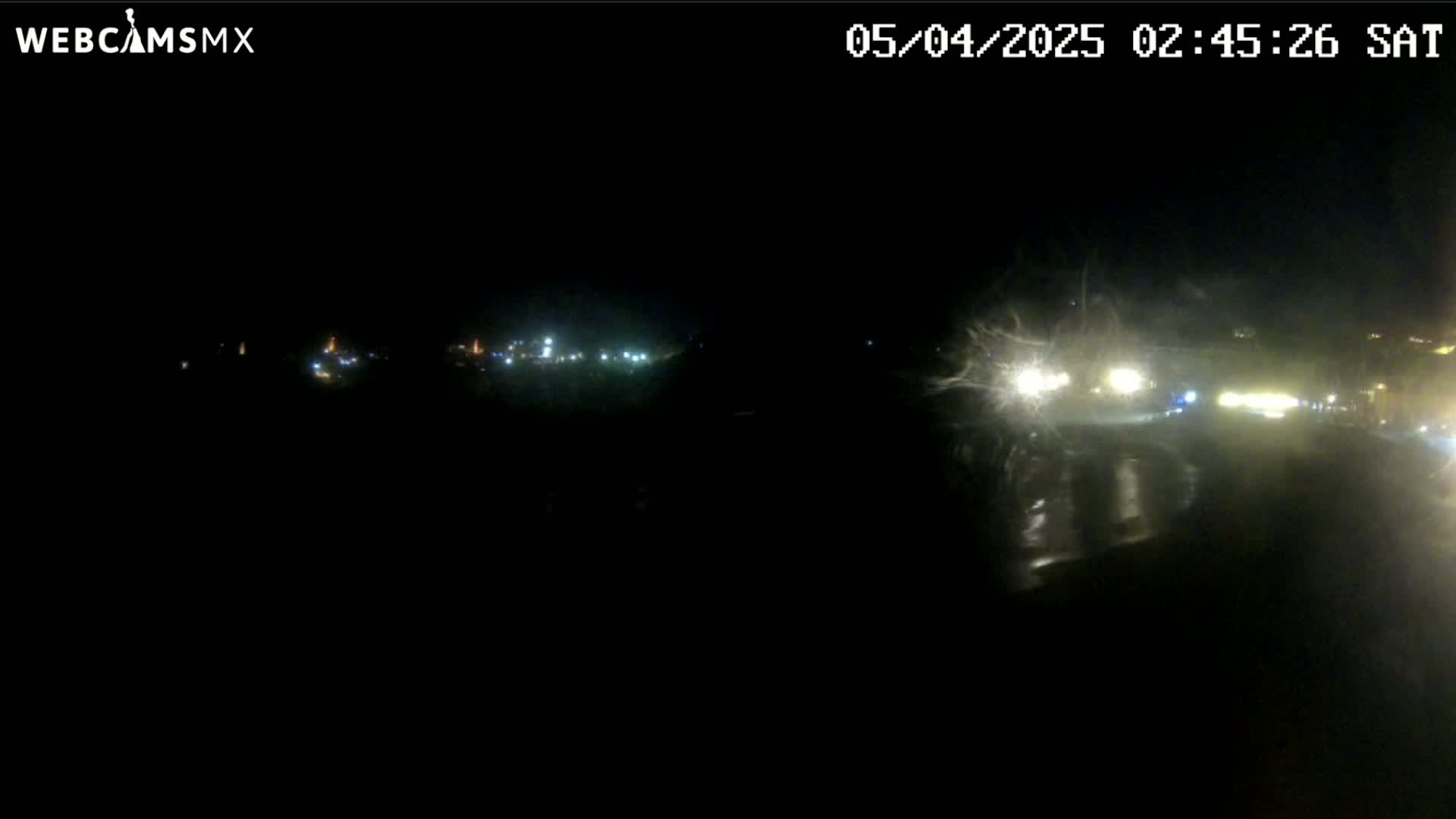 A nighttime, rain-splattered view of a road with distant lights and vehicles.