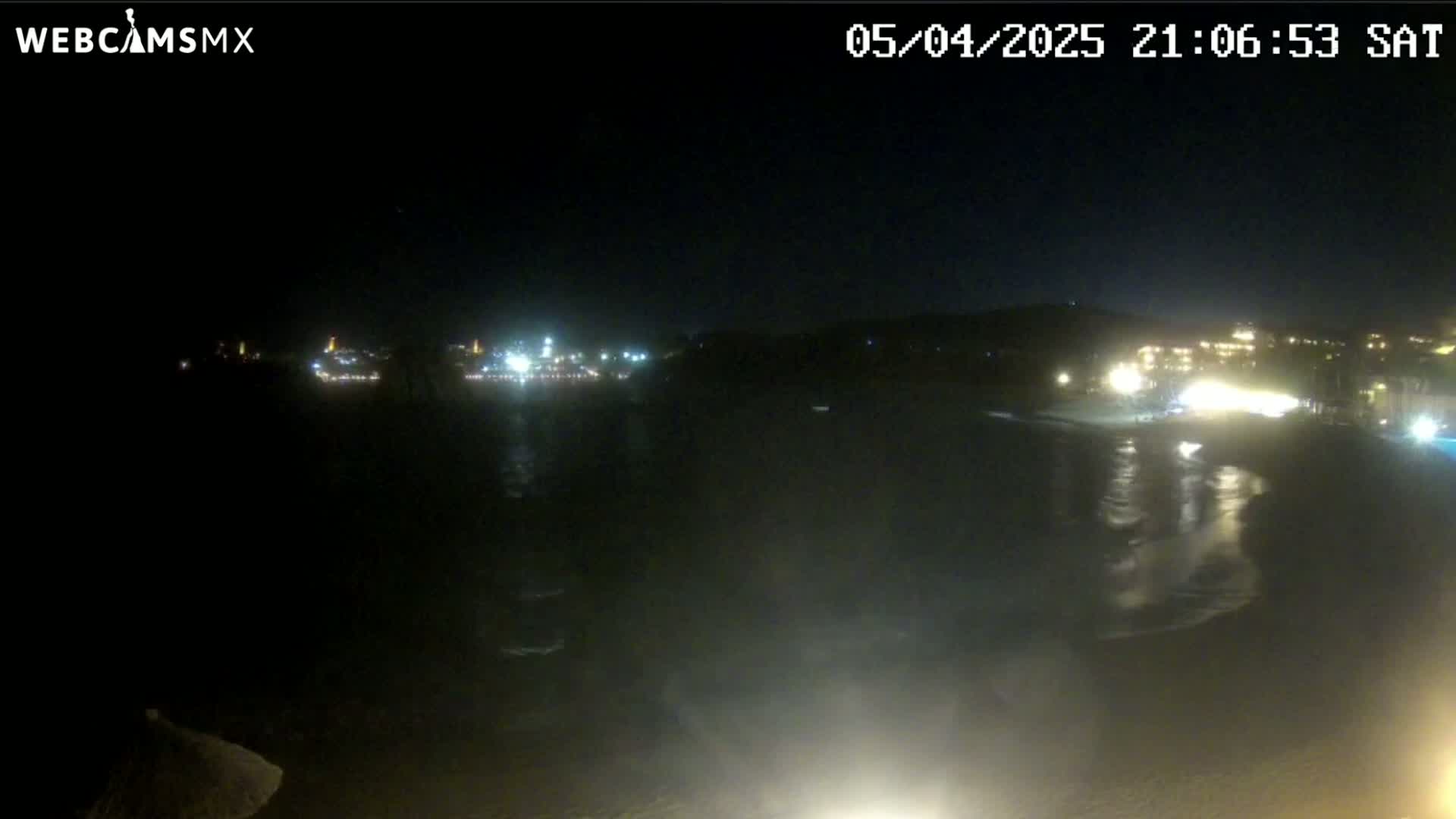 A nighttime, low-light view of a dark body of water reflecting the lights of a distant shoreline.