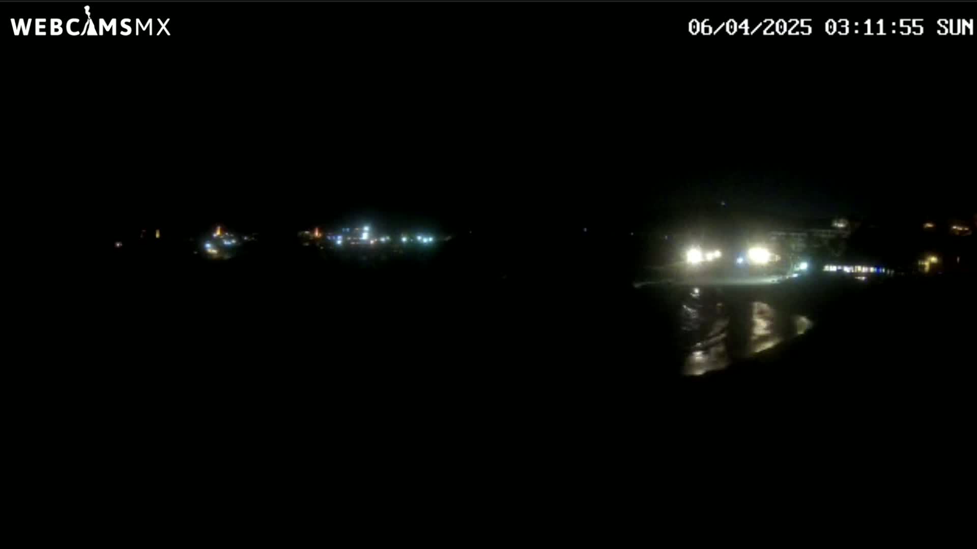 A dark, nighttime scene shows distant lights reflecting on a body of water.