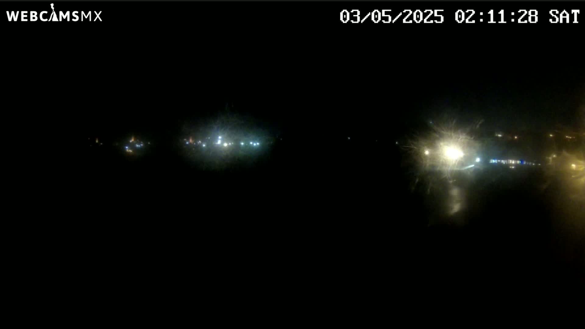 A nighttime long shot shows distant lights from a roadway and buildings, with what appears to be rain or snow obscuring the view.