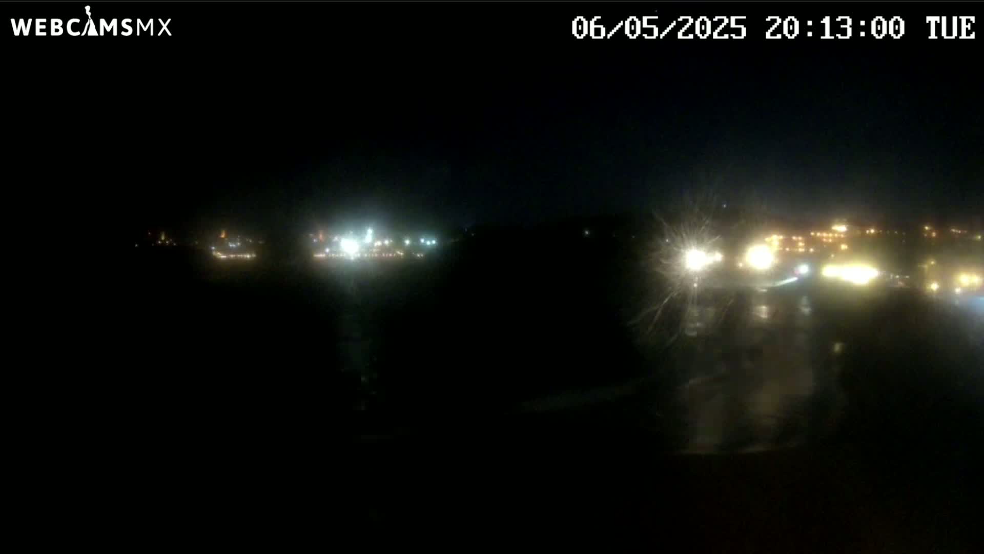 A nighttime long shot of a rain-soaked area with distant city lights visible in the background.