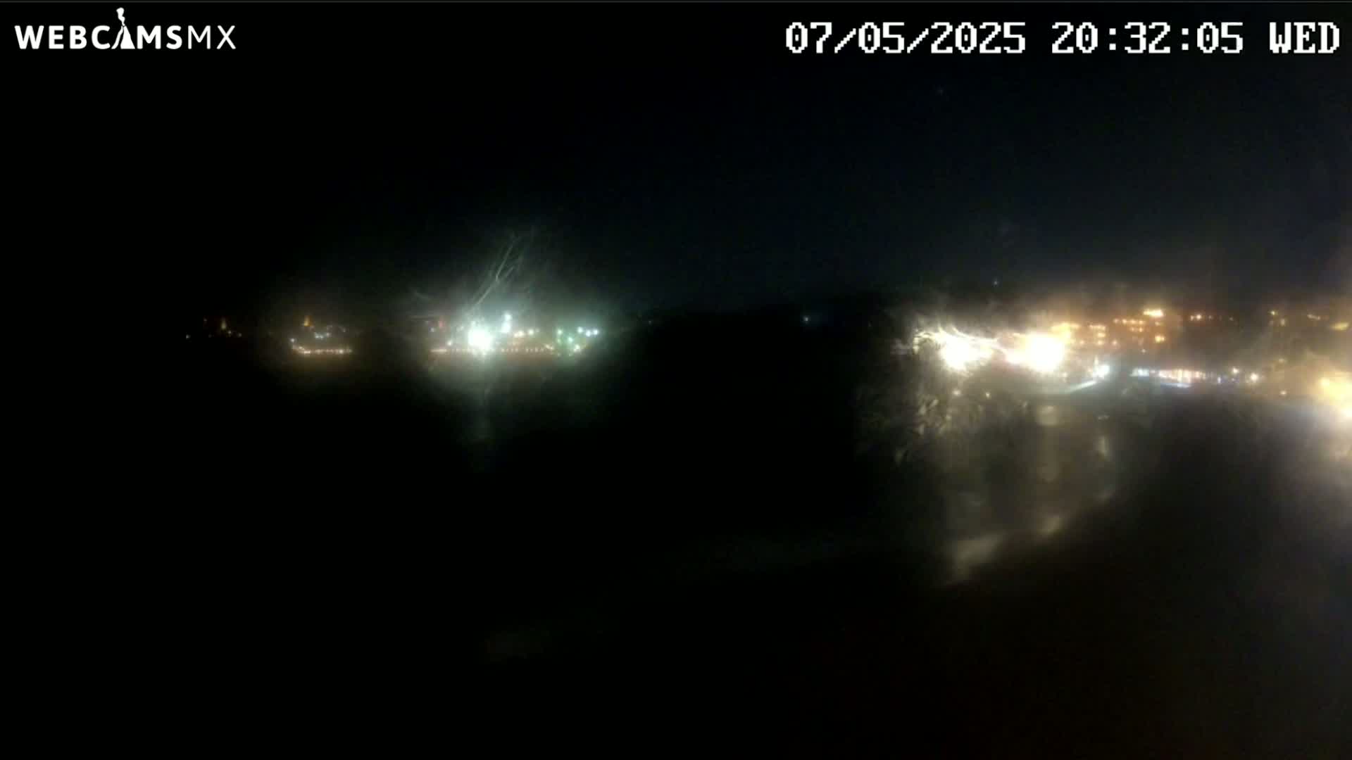 A nighttime, blurry view of distant city lights across a dark, possibly wet, expanse.