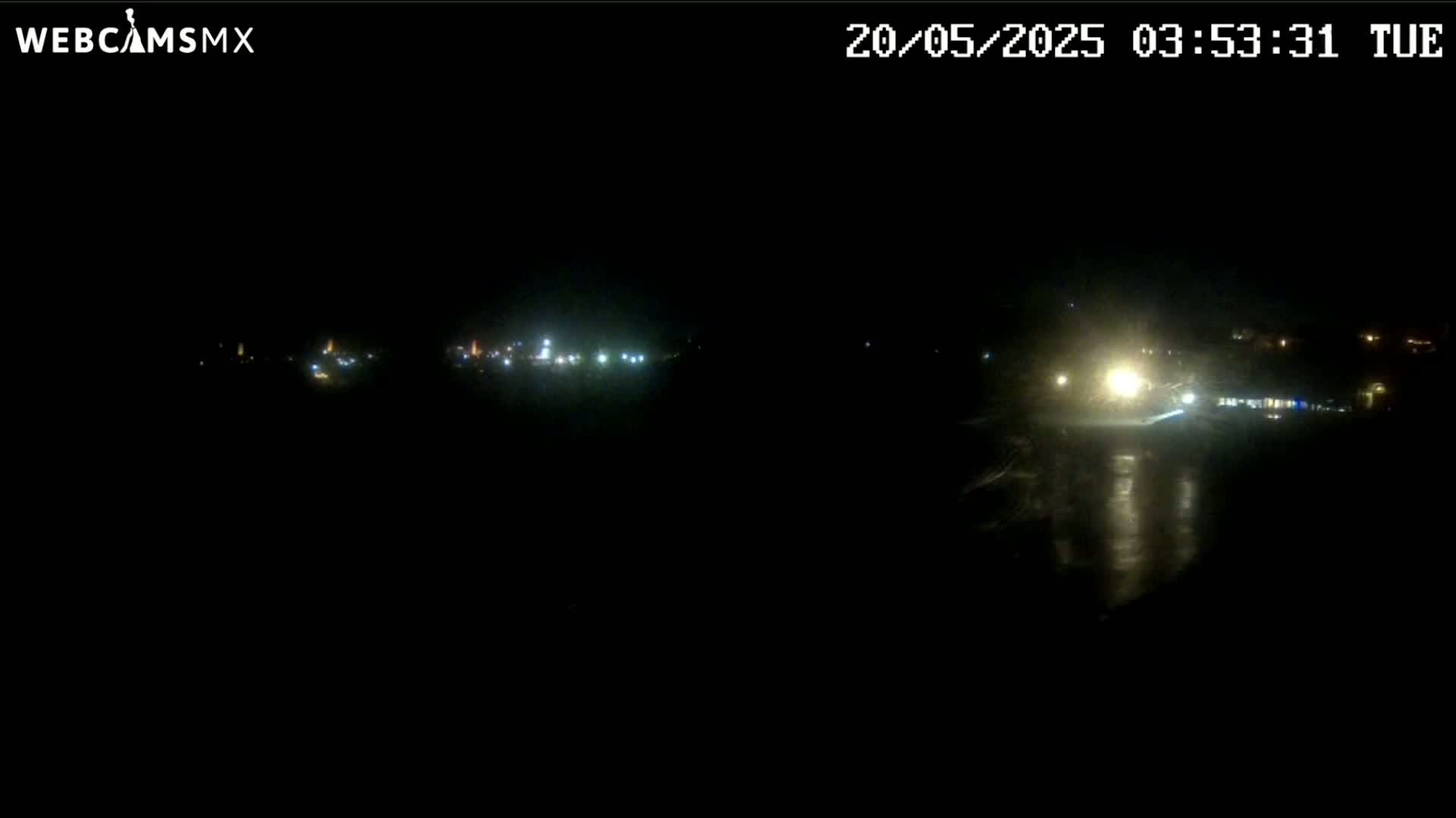 A nighttime, dark scene shows distant lights reflecting on a wet surface.