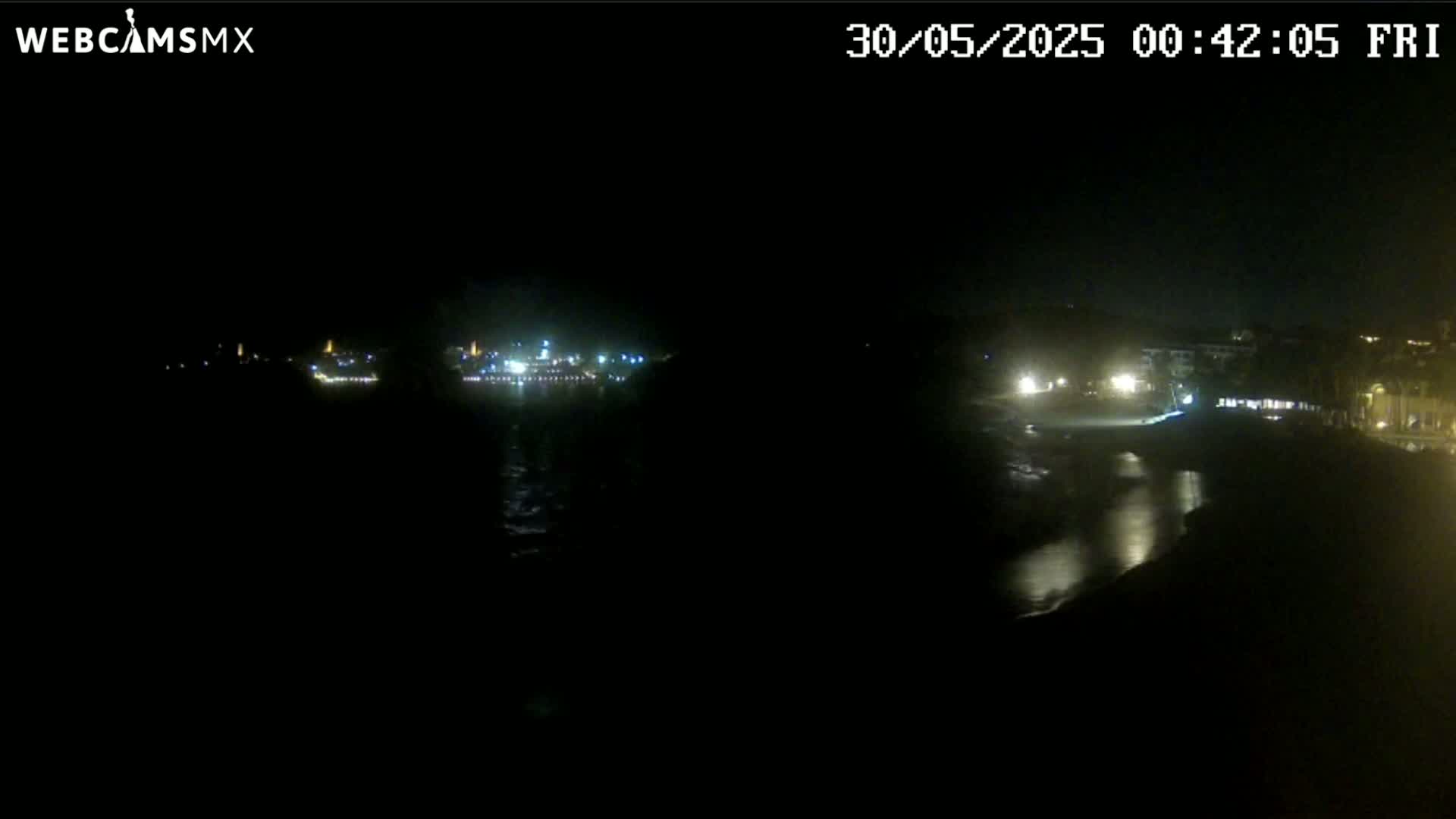 A nighttime long shot shows a dark body of water reflecting the lights of a distant shoreline.