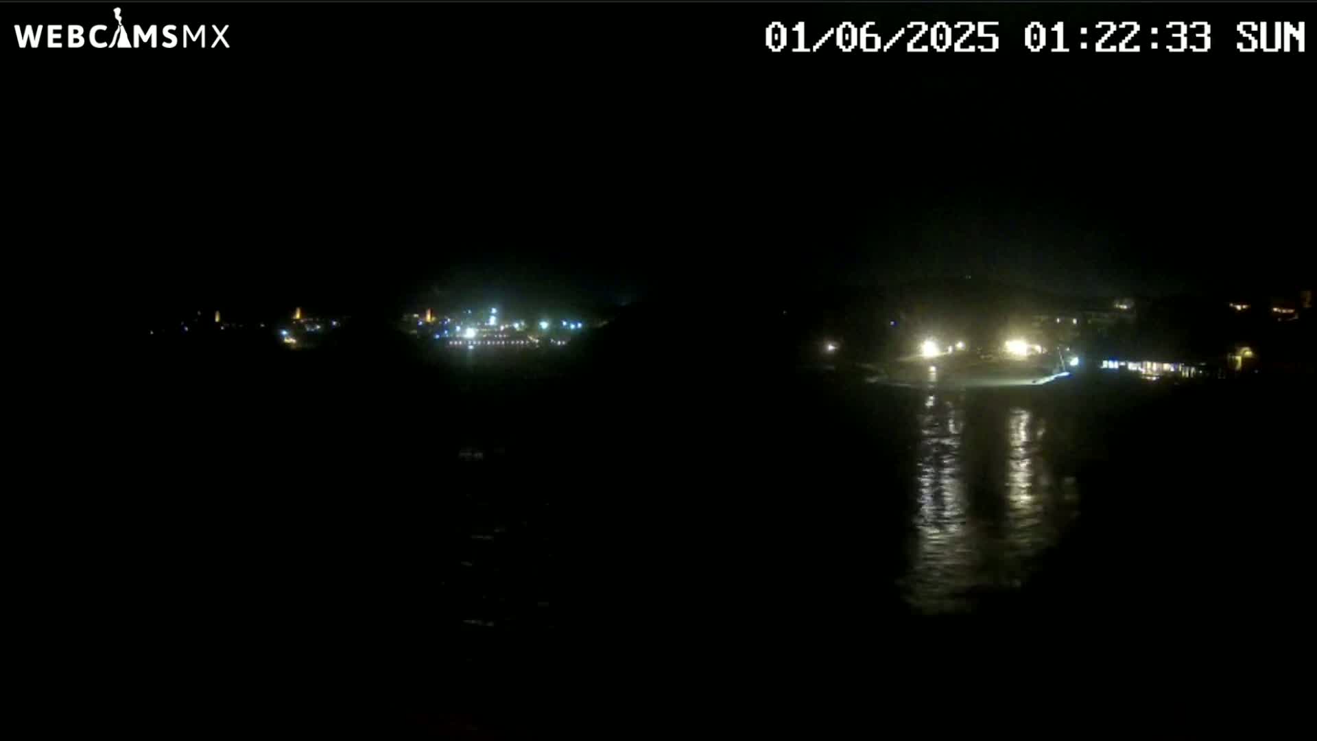 A nighttime view of a dark coastline with scattered lights from buildings and reflections on the water.