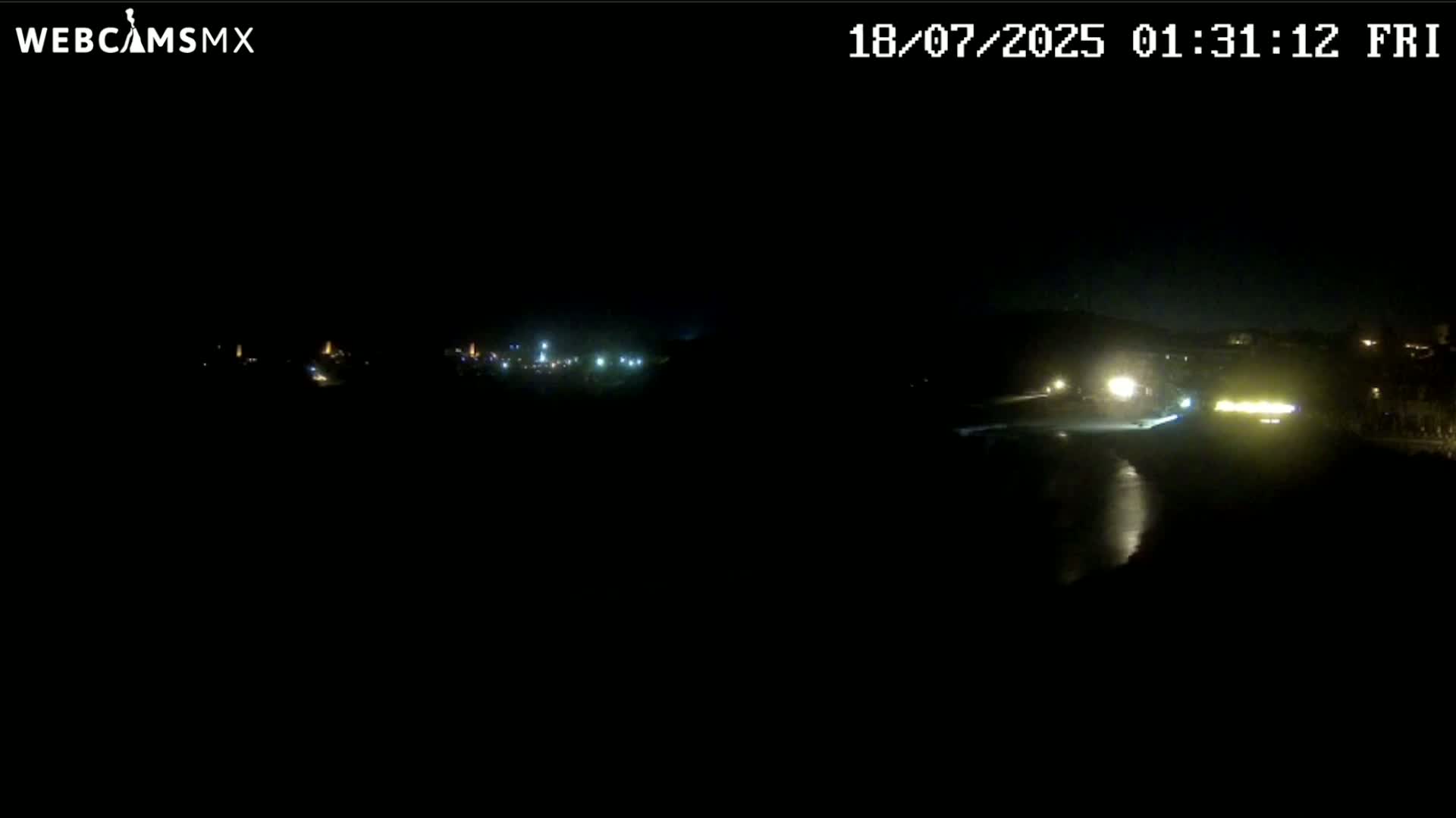 A nighttime, dark view of a dimly lit roadway with a few vehicles and distant lights in the background.