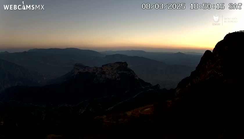 A sunset casts a warm glow over a vast, mountainous landscape.