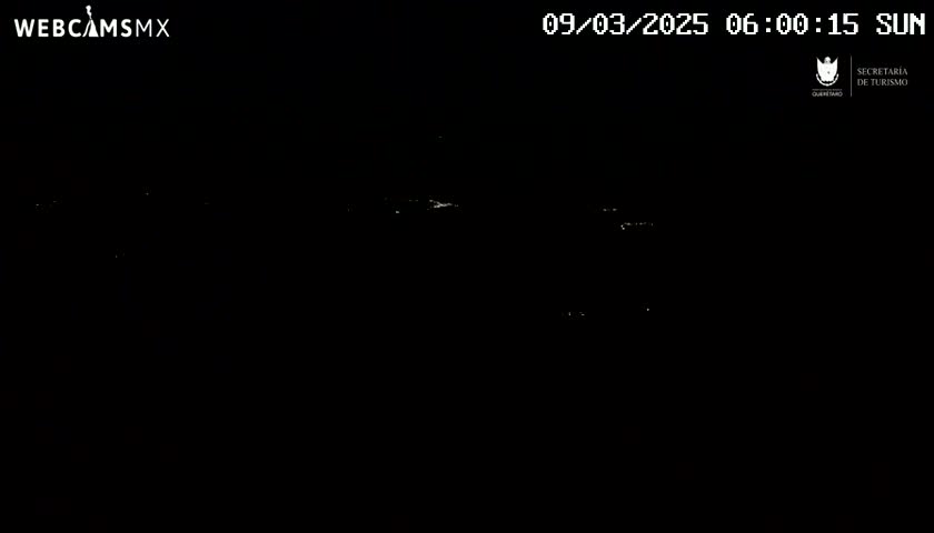A nighttime, dark image shows a few faint lights in the distance under a clear sky.