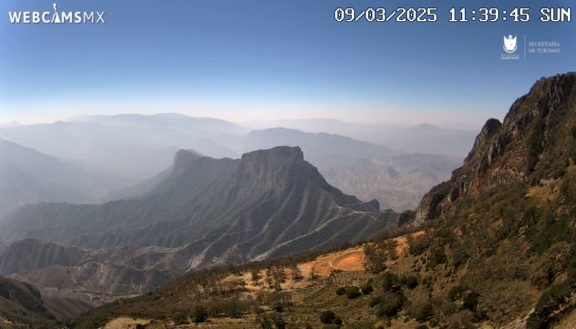 A hazy, sunny view of a vast, mountainous landscape with rocky, arid hillsides and valleys.
