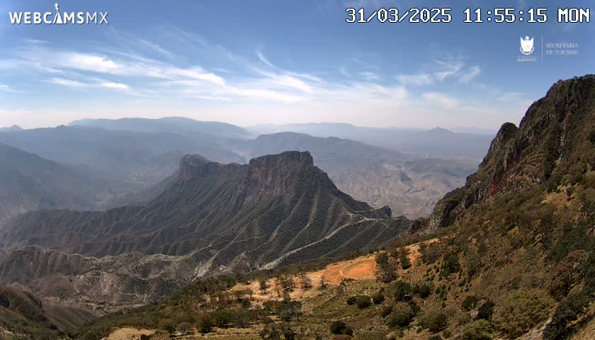 A vast, mountainous landscape under a mostly clear, bright sky stretches to the horizon.