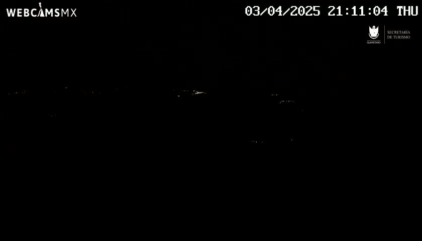 A nighttime, long shot of faintly illuminated distant structures under a dark sky.