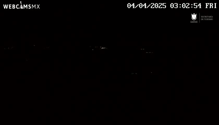 A nighttime, low-light view shows a dark landscape with sparsely scattered pinpricks of light in the distance.