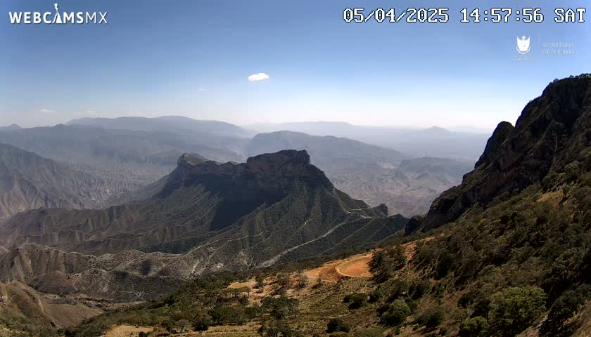 A high-angle view on a clear day shows a vast expanse of rugged, mountainous terrain stretching to the hazy horizon.