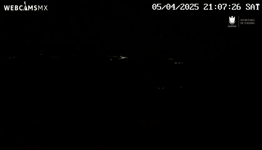 A nighttime, dark scene shows a few faint lights in the distance under a clear sky.