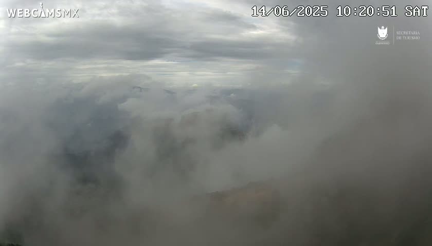 A mostly cloudy, foggy scene is visible from a high vantage point, revealing a landscape obscured by low-hanging clouds.