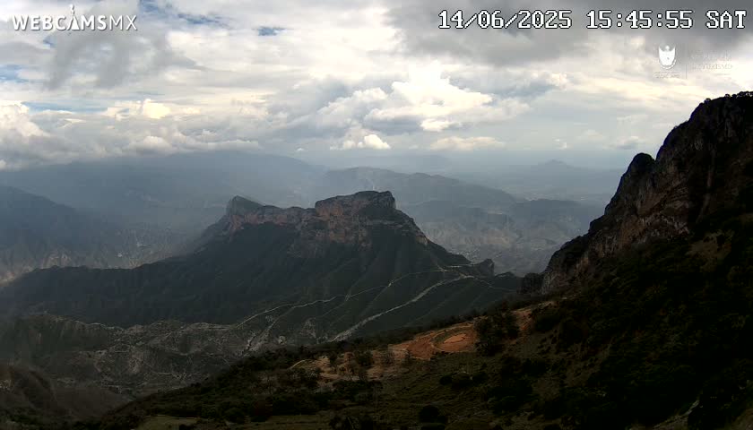 A mostly cloudy, foggy scene is visible from a high vantage point, revealing a landscape obscured by low-hanging clouds.