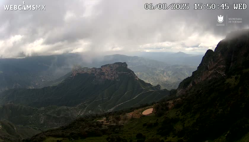A view of a mountainous landscape under a cloudy sky with light rain showering the distant mountains.