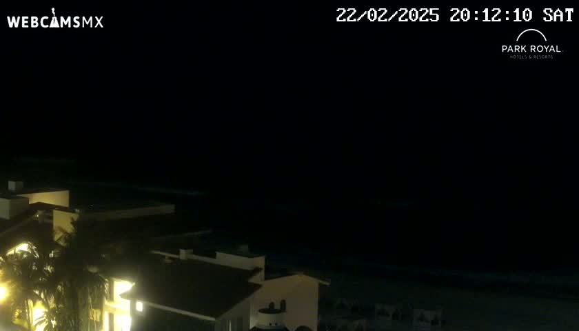 A nighttime view of a beachfront resort, with dark ocean waters and faintly lit buildings.