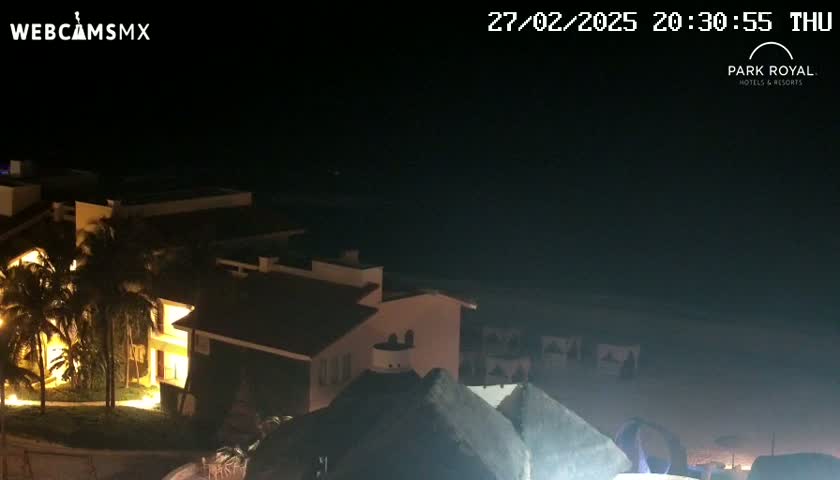 A nighttime view of illuminated buildings near a dark ocean under a clear sky.