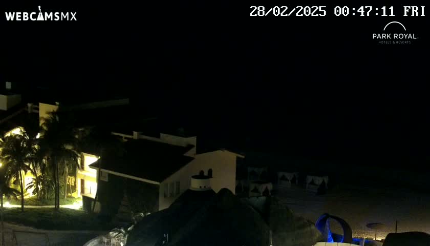 A nighttime view of a brightly lit resort complex near a beach under a clear, dark sky.