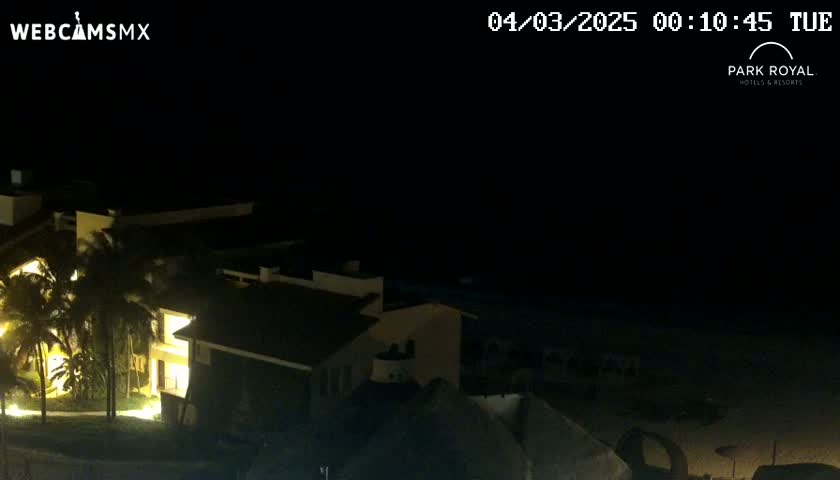 A nighttime view of a resort building complex near a dark beach under a clear, starless sky.