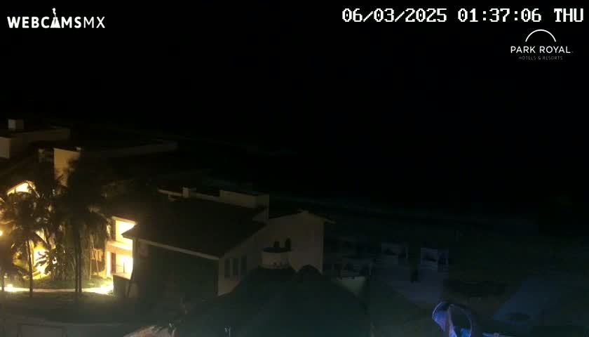 A nighttime view of a brightly lit resort building near a dark ocean under a clear sky.