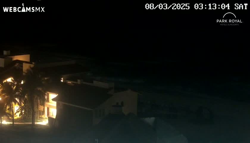 A nighttime view of a brightly lit building complex near a dark body of water under a clear sky.