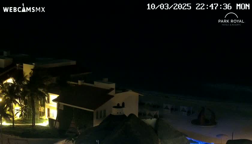 A nighttime view of a resort complex near a beach under a clear, dark sky.