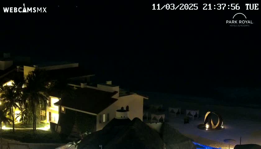 A nighttime view of a resort illuminated against a dark, clear sky overlooking a beach.