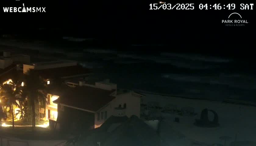 At night, a brightly lit building overlooks a dark ocean with gently moving waves.