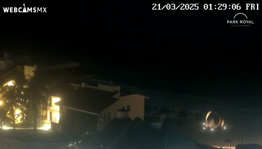 A nighttime view of a brightly lit building near a dark beach under a clear sky.